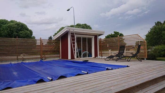 Nyinstallerad vindskiveplåt på ett litet rödväggt poolhus med öppen terrass och en stege lutad mot taket.