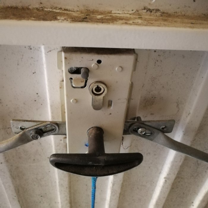 Närbild av garagedörrs mekanism med band och spak under smutsigt tak.