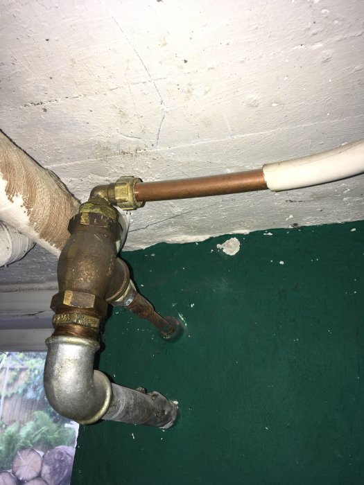 Gamla ventilen och rör vid en vägg, med synliga skruvställen och tecken på åldring.