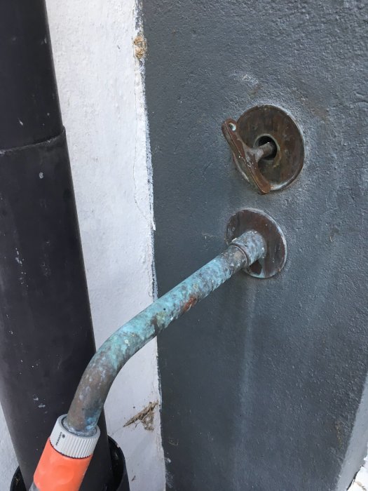 Gammal rostig ventil och vridstång på en gråstrukturell vägg med vit kant.