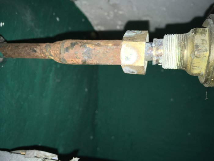 Närbild av en rostig vridstång ansluten till en ventil, med några muttrar och synliga gängor.