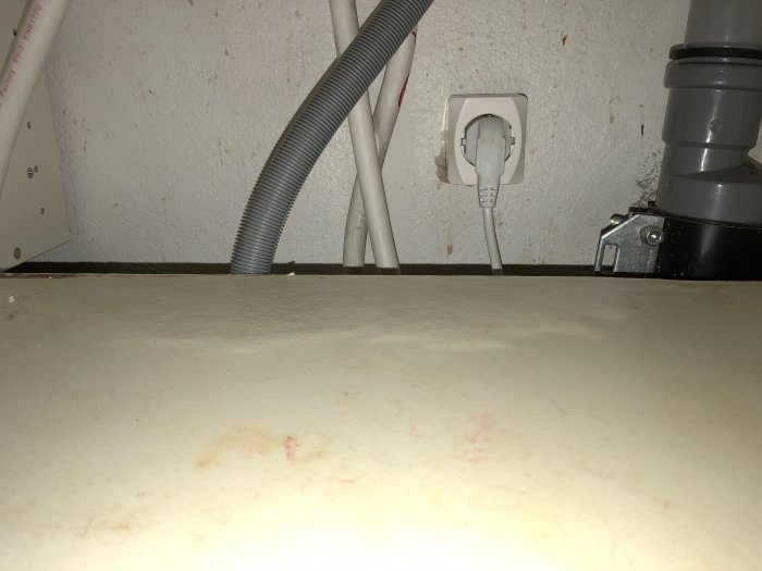 Vattenledningar och eluttag under bänkskåp indikerande en vattenskada med möjlig mögelbildning.