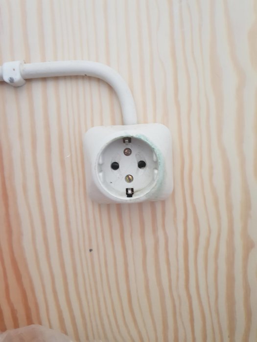 Jordat vägguttag monterat på träpanel med ansluten kabel.