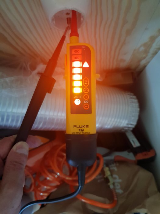 En Fluke T90 spänningsprovare hålls mot en kabel, med lysande indikatorljus som visar spänningsnivån.