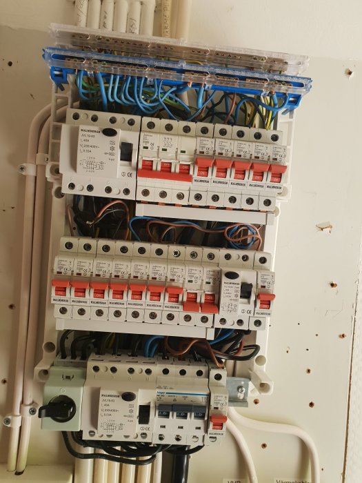 Elektrisk säkerhetspanel med flera säkringsbrytare, och ledningar monterade på en vägg.
