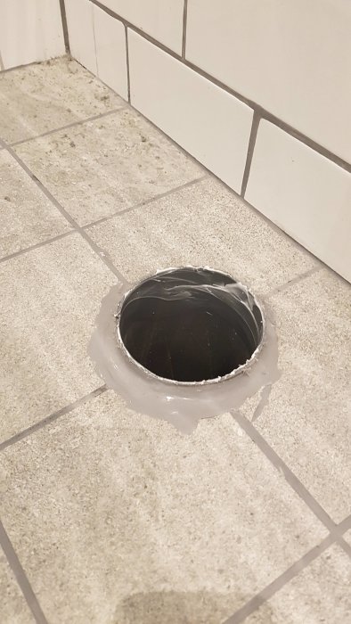Monterad manchett runt rör i golv med felplacerad fläns och silikon, nära väggtillslutning.