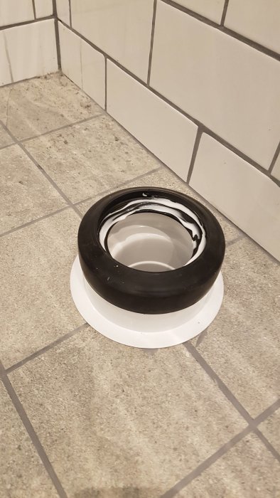 En toalettfläns och gummitätning installerade på ett golv med kakel och klinkers.