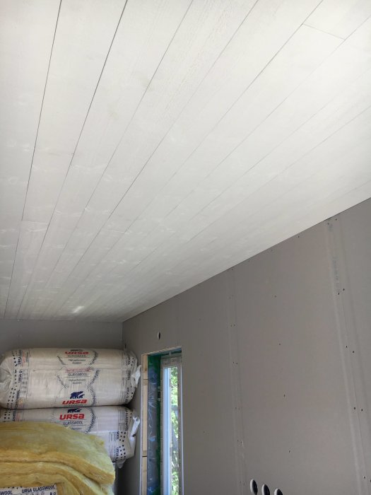 Nymålad vit innertakspanel i ett rum under renovering med oisolerade väggar och isoleringsmaterial.