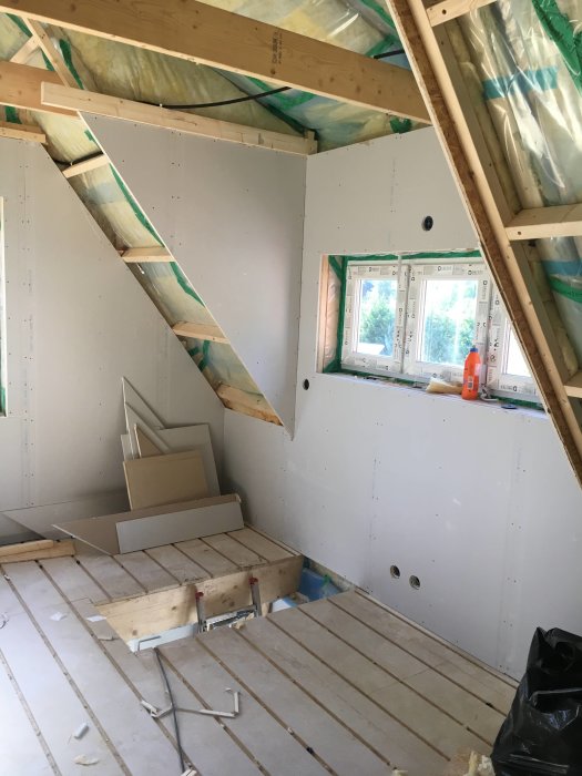 Renoveringsarbete i ett rum med isolering synlig och väggskivor delvis installerade.