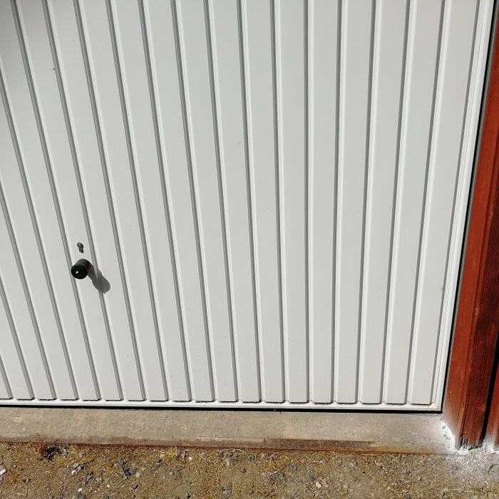 Vit garagedörr utan synlig hänglåsanordning, endast med dörrhandtag och nyckelhål.