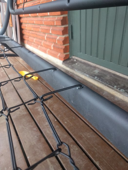 Ej komplett hammocknät fastsatt med stålkrokar på metallram mot trä och tegelbakgrund.
