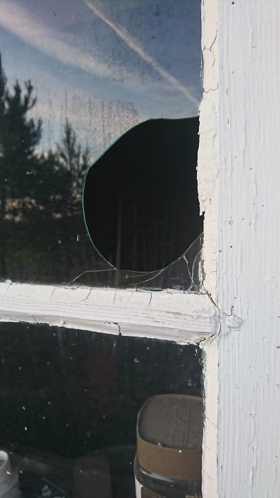 Ett fönster med ett runt, trasigt glas där en del saknas och skarpa kanter syns.