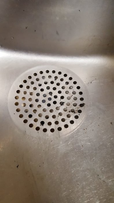 Närbild på ett rostfritt diskbänksfilter med många hål, indikerar fråga om avloppsmått för anslutning.