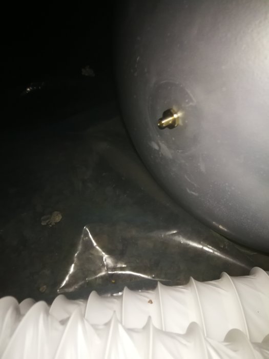 En hydrofortank nära bild med en synlig luftventil och del av en vit strukturerad yta, belyst i ett mörkt utrymme.