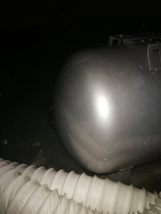 Delvis synlig hydrofor med anslutna vita rör, i ett mörkt och suddigt foto.