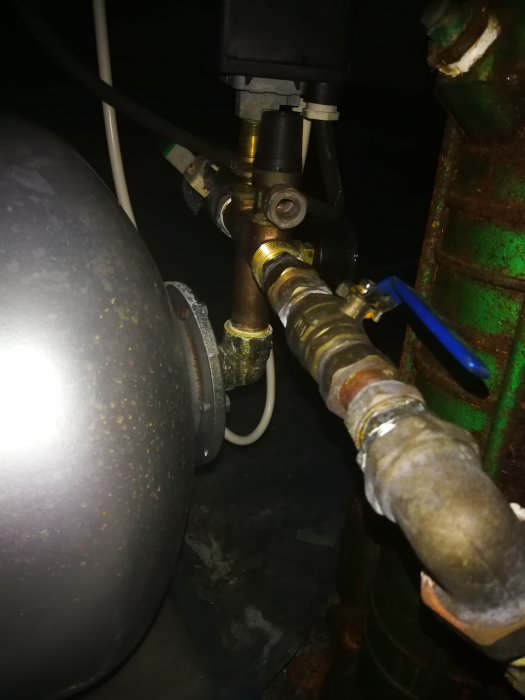 Närbild på anslutningar till en hydrofor med kopparledningar och en del korrosion, i dunkelt upplyst rum.