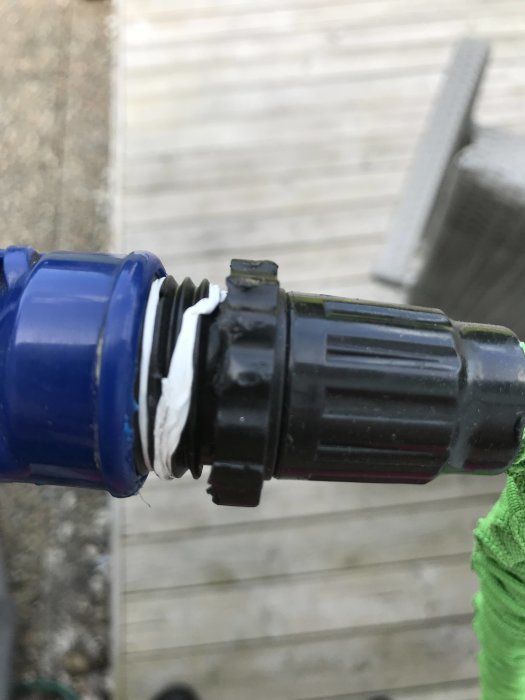 Närbild av en vattenslangs ände med en inre gängad koppling och en defekt del, på en träaltan i bakgrunden.