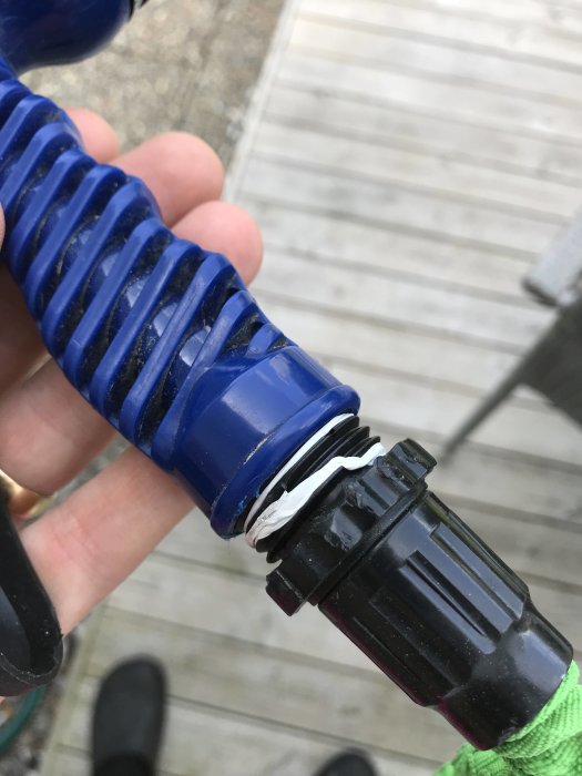 Ihoprullad blå vattenslang med en svart koppling och inre gänga på munstycket som hålls i en hand.