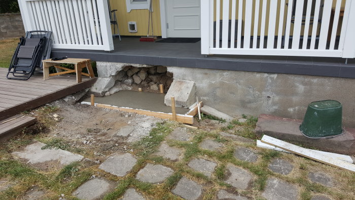 Nygrävt och gjutet fundament för trappan vid hus, med sten och byggmaterial synligt.