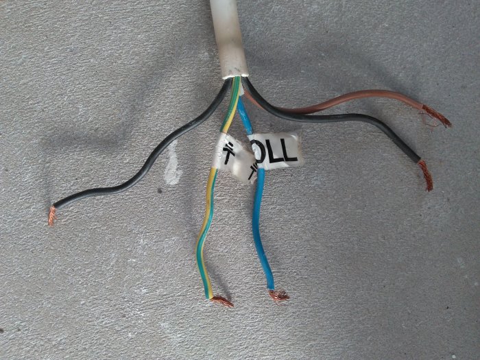 Elektrisk kabel ändar med kabelskor och märkning, på ett betonggolv.