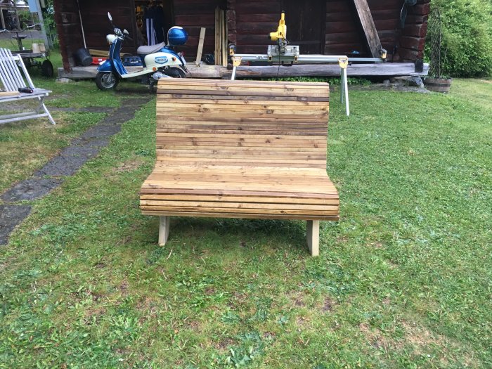 Nybyggd liten träbänk på gräsmatta framför en stuga och skoter.