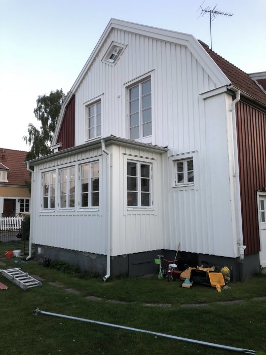Vit trävilla med veranda och gammal grundmur som behöver putsas.