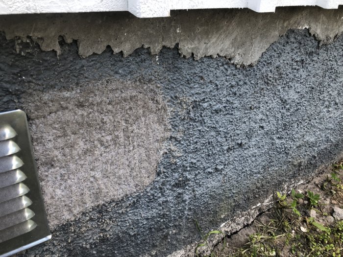 Närbild av en grundmur från 1930 med sparsamt cement och stora stenar, delvis täckt av en tunn slammning och sockelfärg.