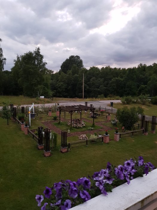 Vy över en nyanlagd park med planterade blommor, staket, pergola och gräsmatta från ett balkongperspektiv.