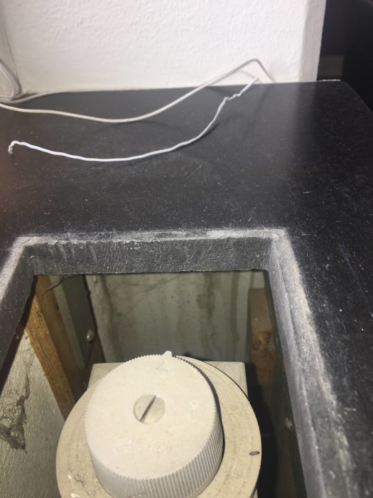 Hål i skiva där ventil tagits bort för att dra kablar, med damm på kanterna och liggande ventil vid sidan.