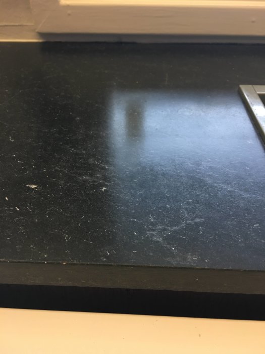 Närbild på en svart bänkskiva med ljusa repor och en träkant i nedre delen av bilden.
