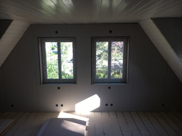 Nyuppsatt panel och smyg runt två fönster i ett halvfärdigt sovrum med lutande tak.