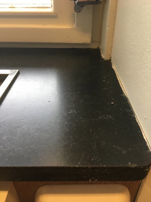 Svart bänkskiva med diagonala mönster övre halva och horisontella streck nedre halva vid fönster.