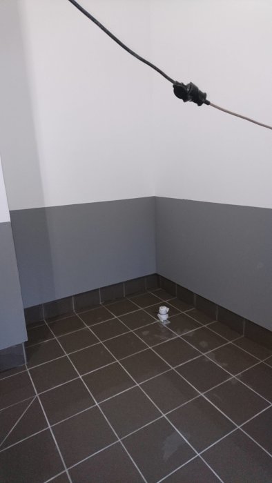 Mörkbruna klinkerplattor på ett golv i ett hörn med grått målade väggar.