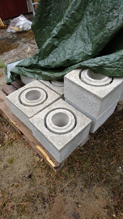 Nyinköpta skorstenar av betong stackars på en pall, täckt delvis av en grön presenning.