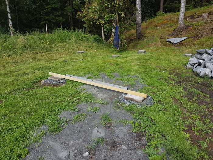 Betongplattor utspridda på gräsmark som förberedelse för placering av container, med gräs och träd i bakgrunden.