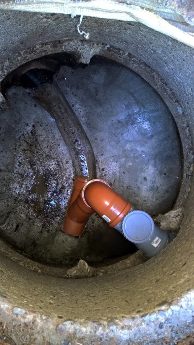Betongbrunn med nygjuten ränna och installerad avloppsröranslutning, visar anslutet grått och brunt rör.