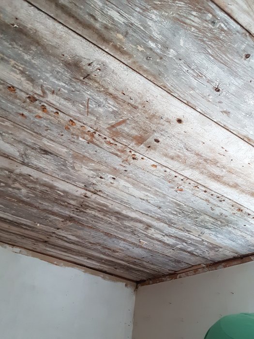 Äldre, slitet träbjälklag synligt i ett tak som ska renoveras, med spår av färg och skador.