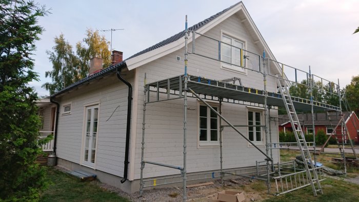 Hus under renovering med ställningar, nya fönsterplåtar, fodring och dekorativa takbalkar som liknar den äldre delens gavel.