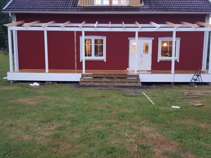 Nybyggd trätrappa med reglar och nymålade stolpar framför röd husfasad och vit veranda under konstruktion.