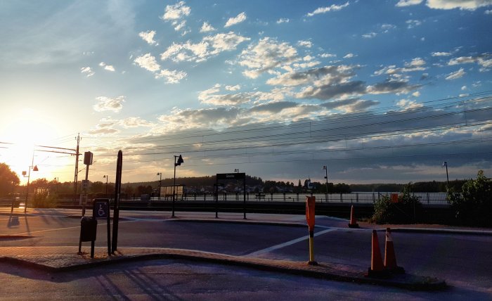 Skymning vid Gnesta tågstation med solnedgång, moln och trafikskyltar.