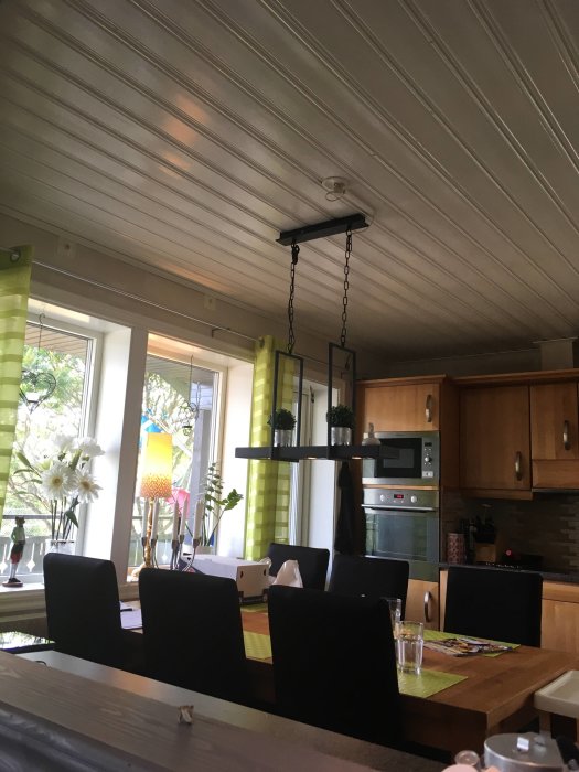 Nyinstallerad kökslampa över matbord, med träpanel i taket och köksskåp i bakgrunden.