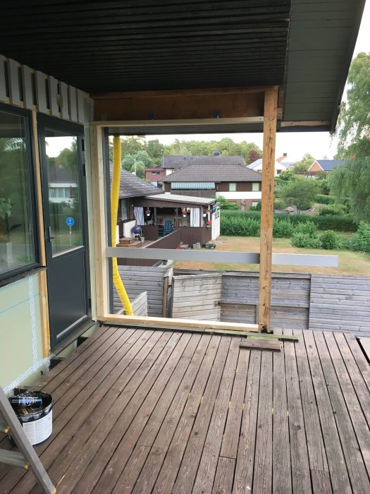 Obyggd altan med stolpar och träplankor, öppning i vägg, utsikt över bostadsområde, färgburk på golvet.