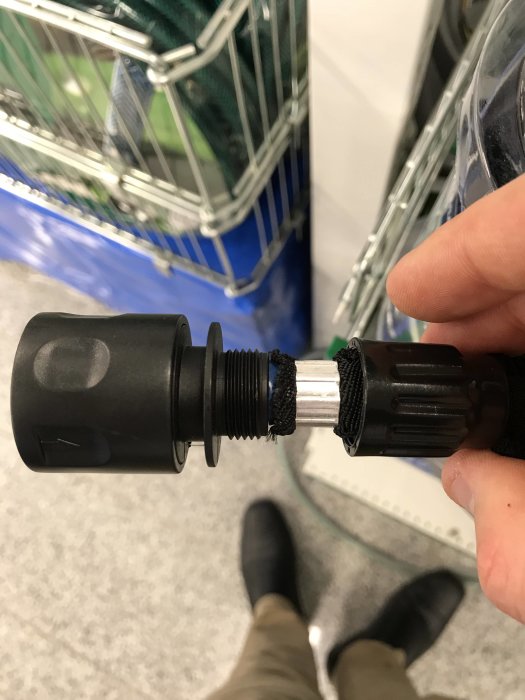Hand håller en byggdetalj framför en varukorg i butik.