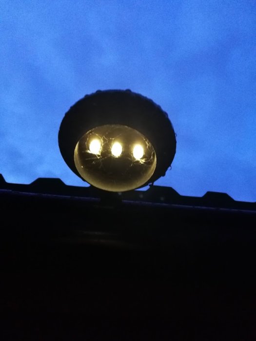 Tänd lampa mot mörk himmel under regnig dag, fäst vid takkant.