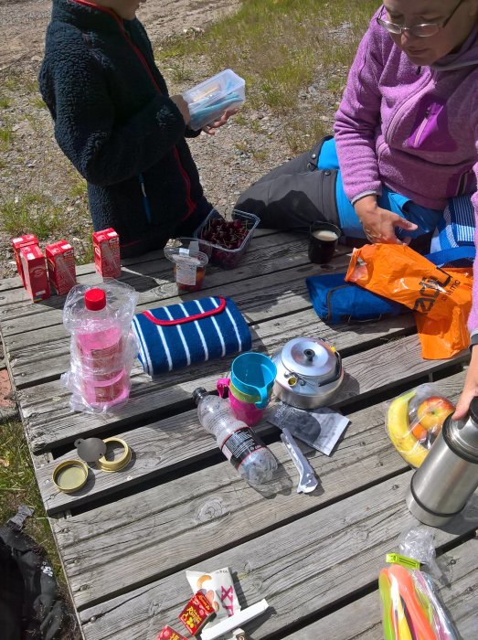 Oreda vid en picknick med kaffe, frukt och tillbehör på ett träbord utomhus.