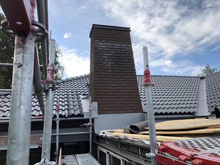Tegelskorsten på tak med pågående installationsarbete av beslag, ställning i förgrunden.