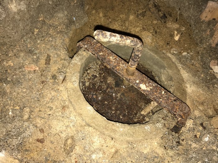 Rostig lucka i ett källargolv med en synlig metallstång, tänkt som renslucka för avlopp.