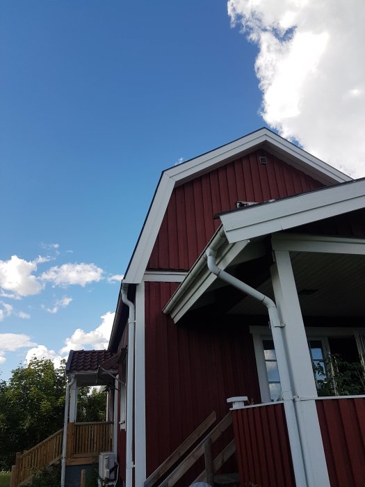 Rödfärgat hus med brutet tak och synlig takfot, samt ventil på gaveln under en klarblå himmel.