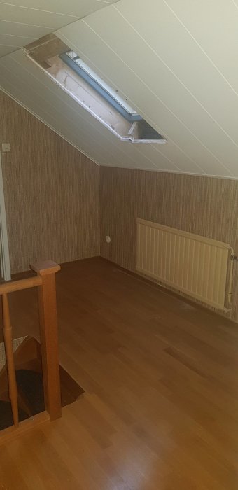 Övervåning före renovering med snedtak, trägolv, och ett öppet takfönster.