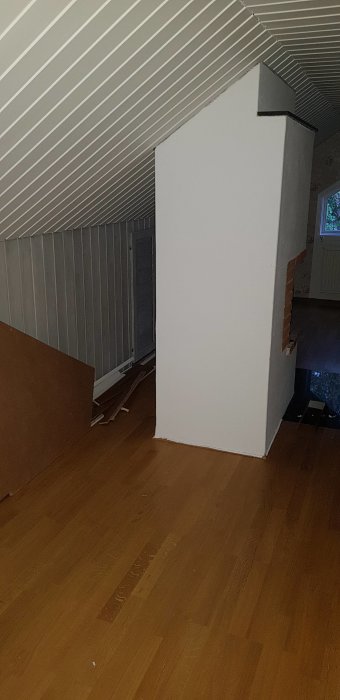 Övervåning under renovering med snedtak och synliga trägolv, väggar och byggskräp.